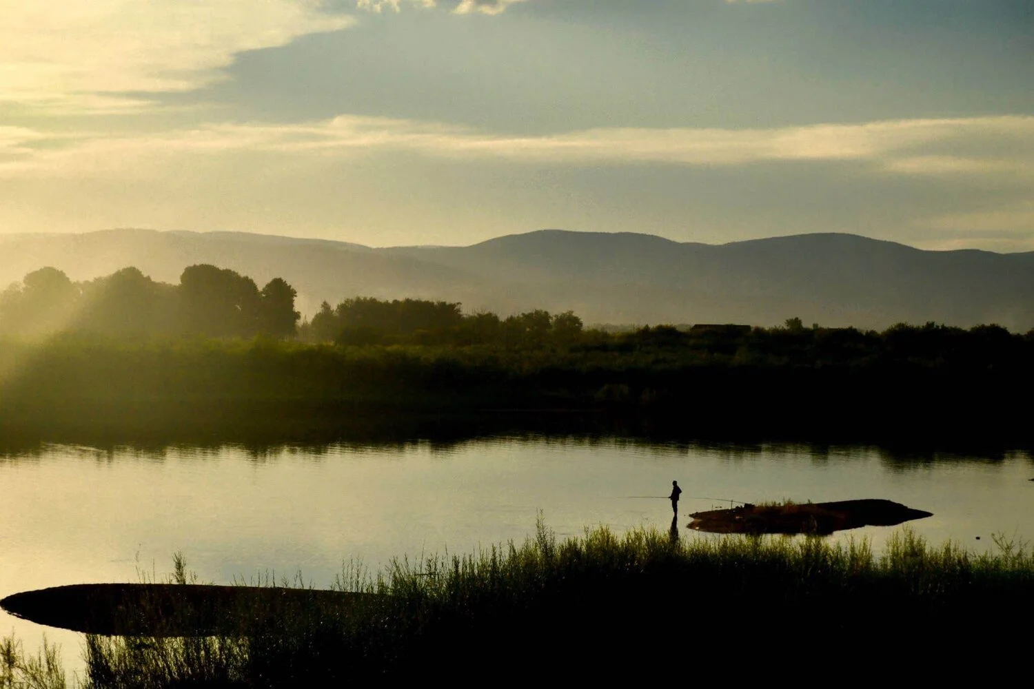 landscape of a lake and a man with fishing rod
